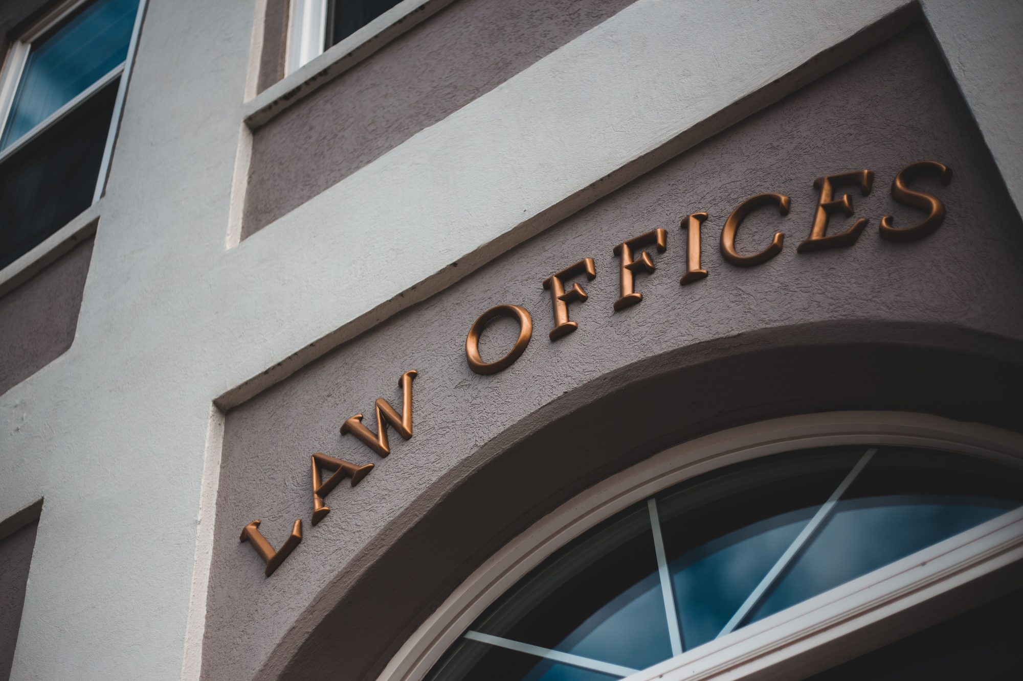 Close-up of a stone building facade with 'LAW OFFICES' lettering in bronze above an arched window entrance.